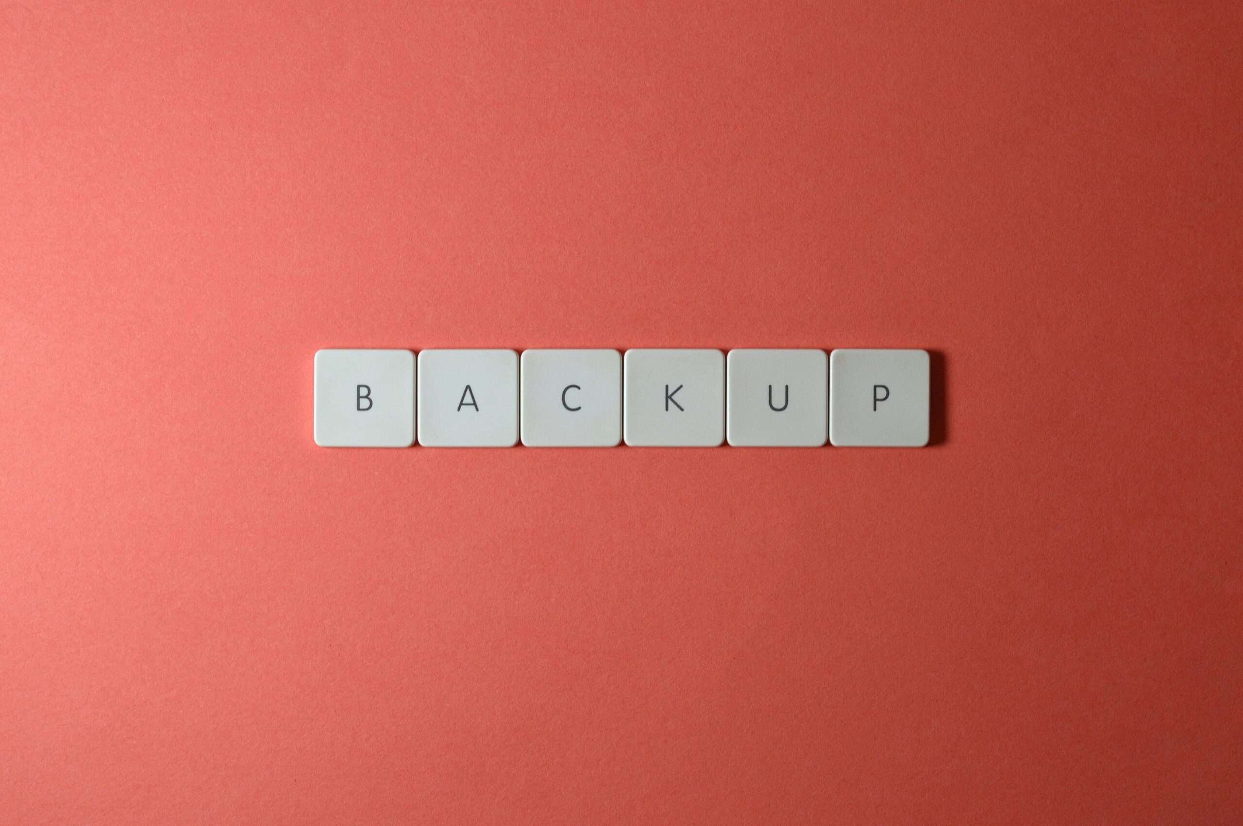 Free Close-up of keyboard keys spelling 'BACKUP' placed on a coral-colored surface. Stock Photo