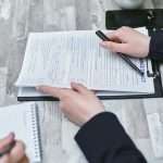 Free Close-up of hands analyzing insurance policy paperwork with pen on table. Stock Photo